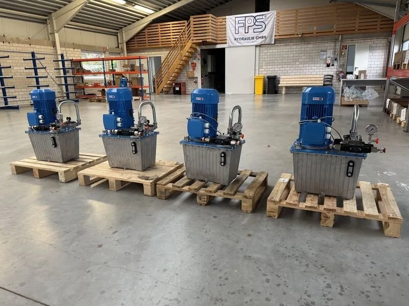 Vier baugleiche Hydraulikaggregate mit blauen Elektromotoren auf Paletten in der Halle