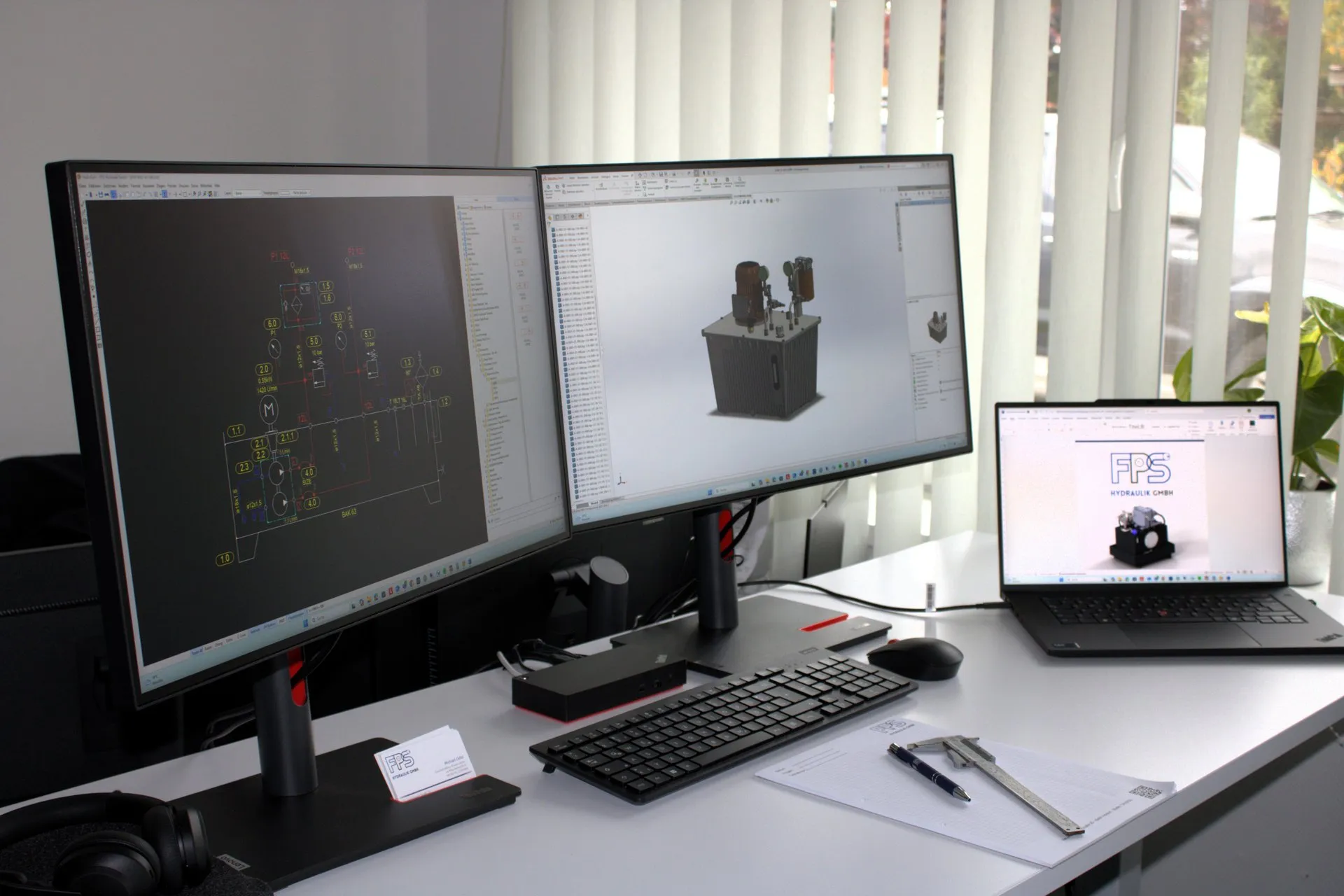 Konstruktionsplatz bei FPS Hydraulik in Holdorf mit zwei Bildschirmen: links ein Hydraulikschaltplan im CAD, rechts ein 3D-Modell, daneben Laptop, Messschieber und Karopapier