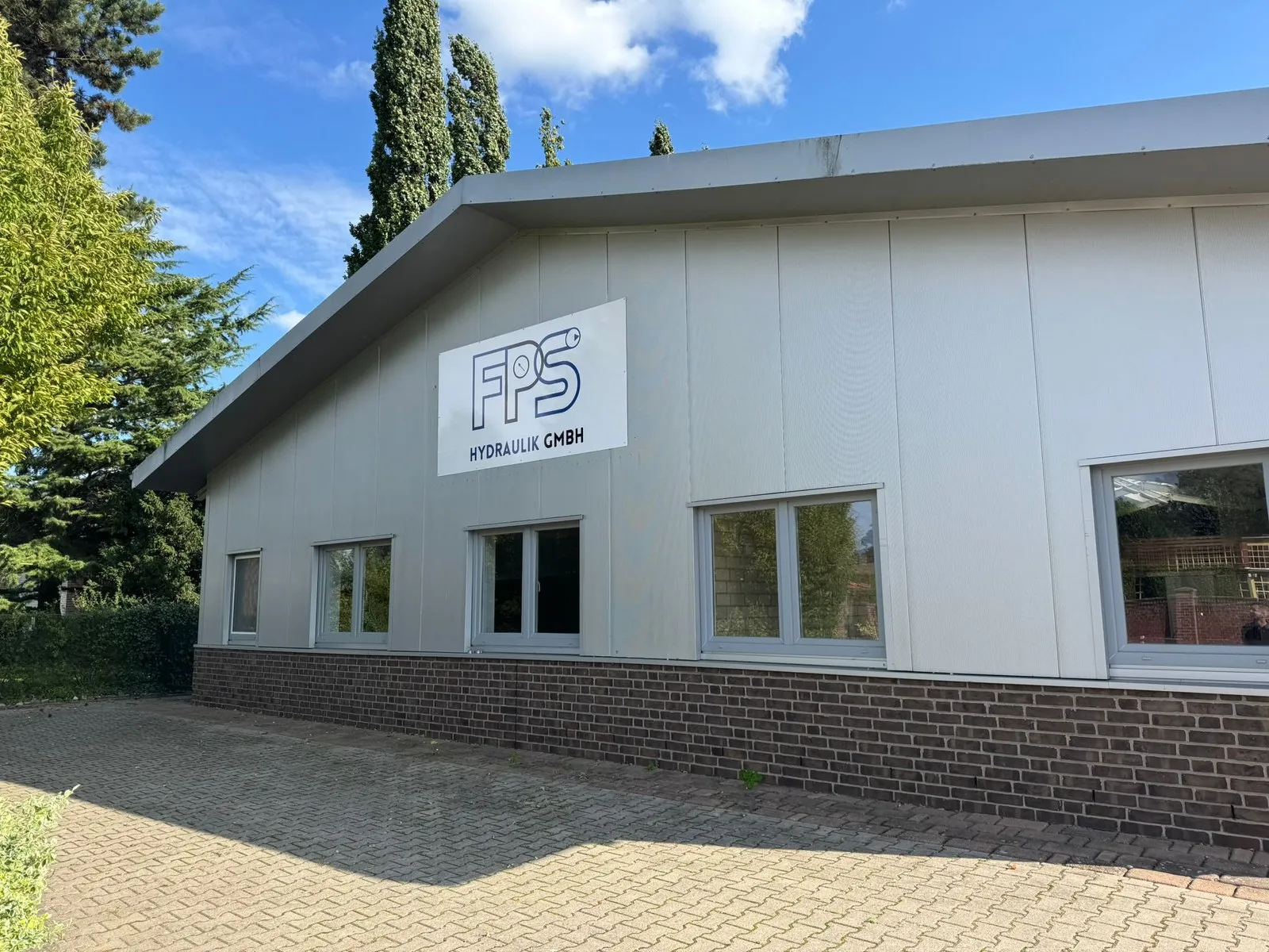 Das Betriebsgebäude von FPS Hydraulik in Holdorf mit Firmenschild an der grauen Fassade